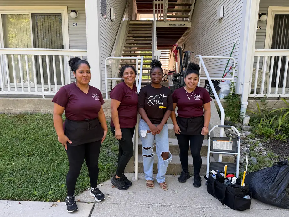 Four Linda Soto Cleaning team members outside an apartment building with a vacuum, a step stool and a supply caddy